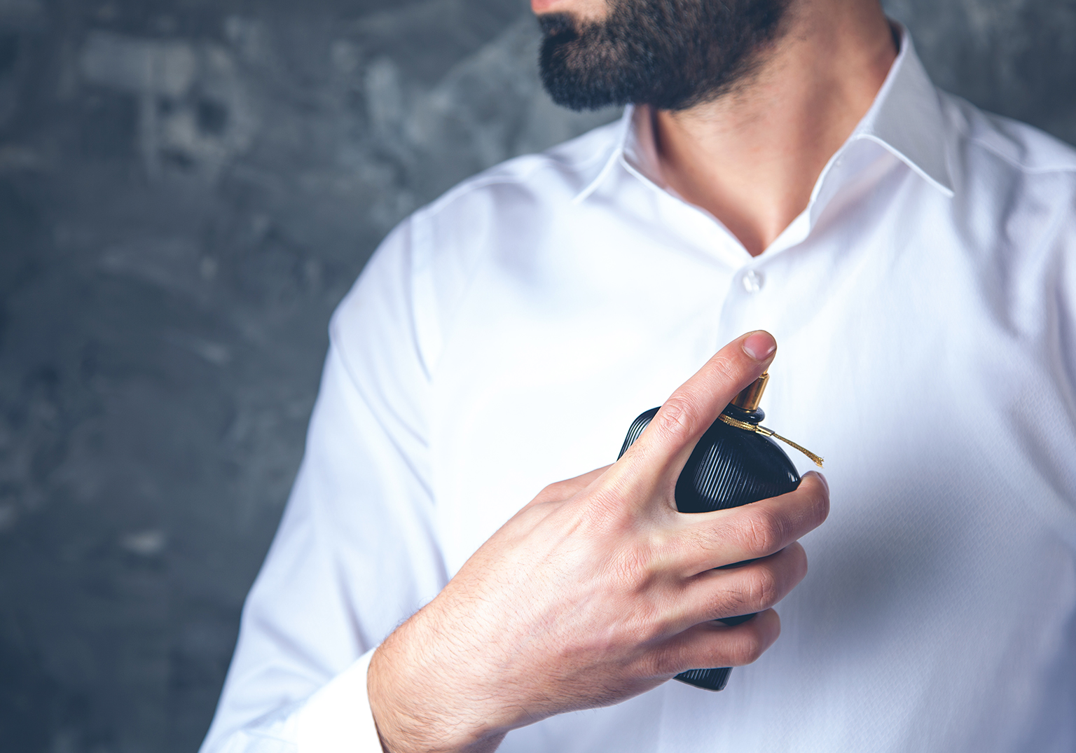 Homem segurando frasco de perfume em camisa branca