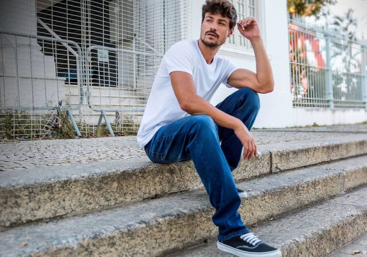 modelo com camiseta branca e calça jeans sentado na escada