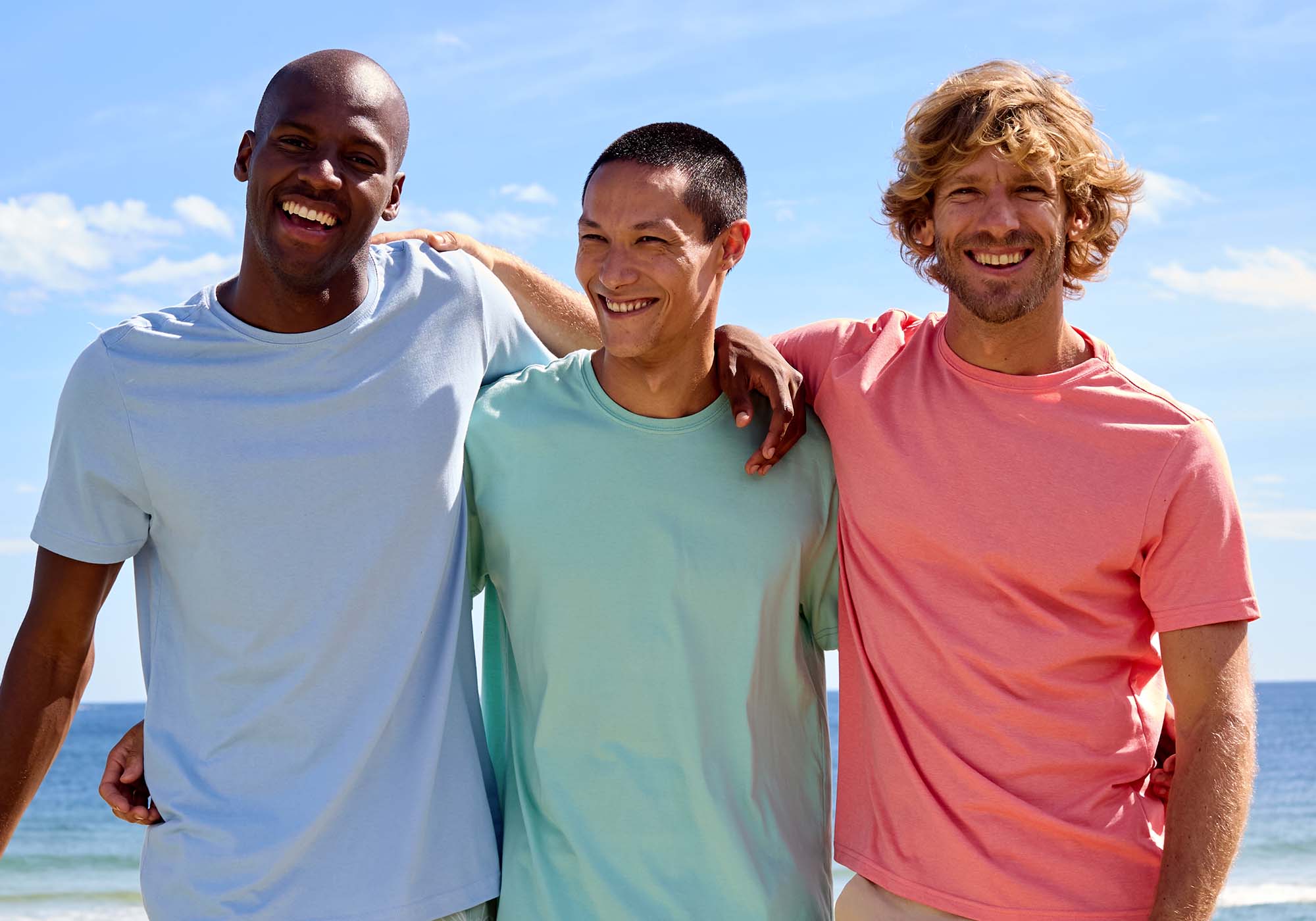 Três homens sorrindo na praia em dias ensolarados