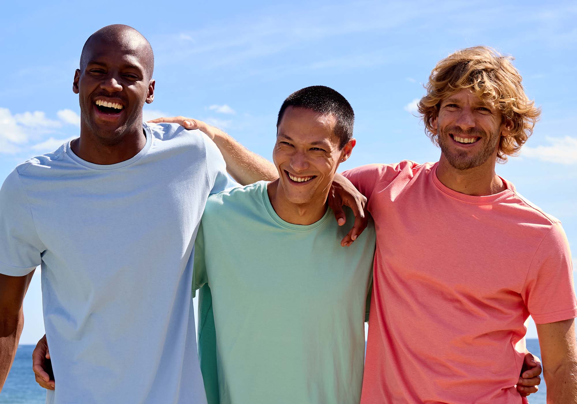 Três homens sorrindo em um dia ensolarado na praia.
