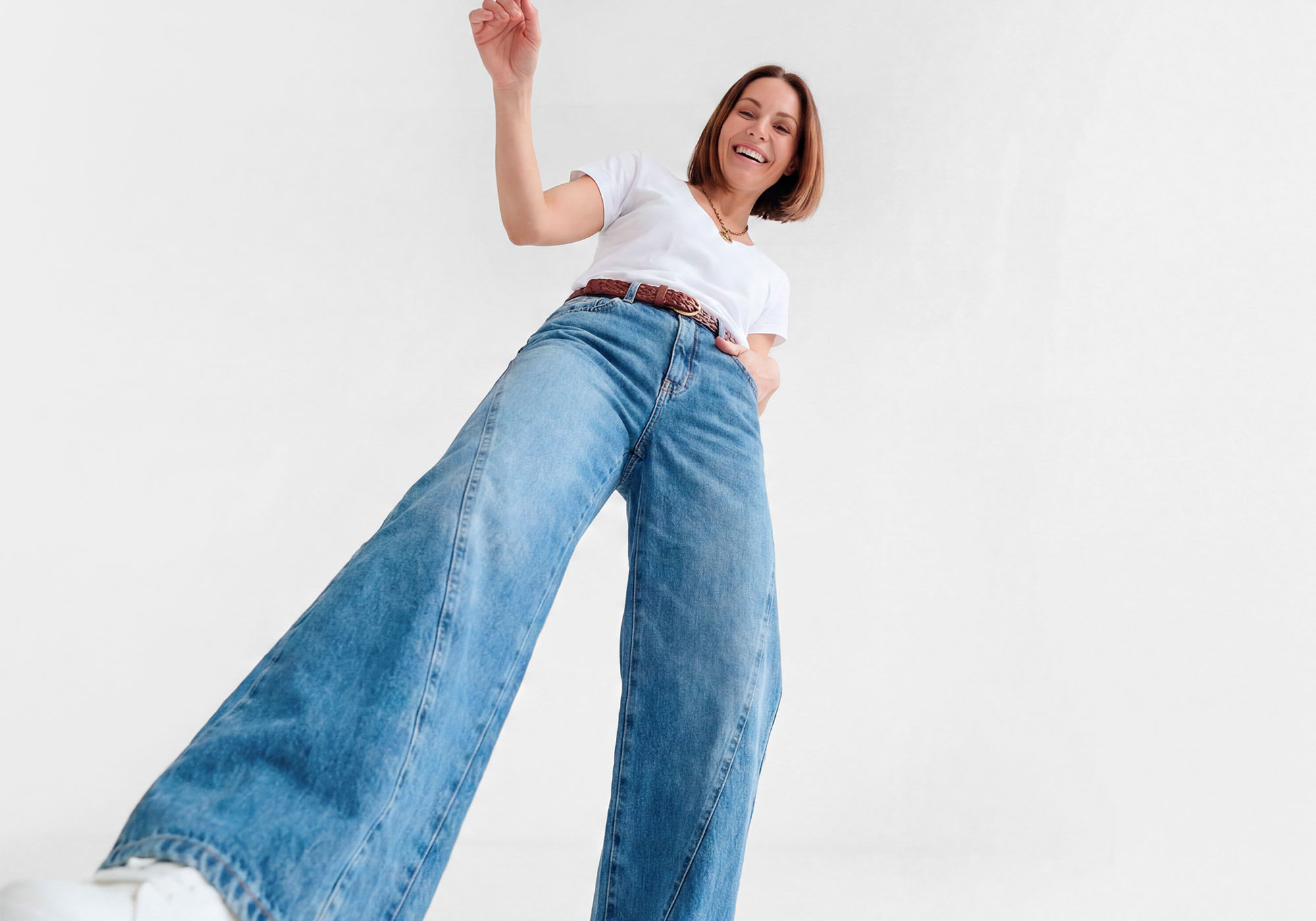 Mulher sorrindo com jeans largos e camiseta branca.