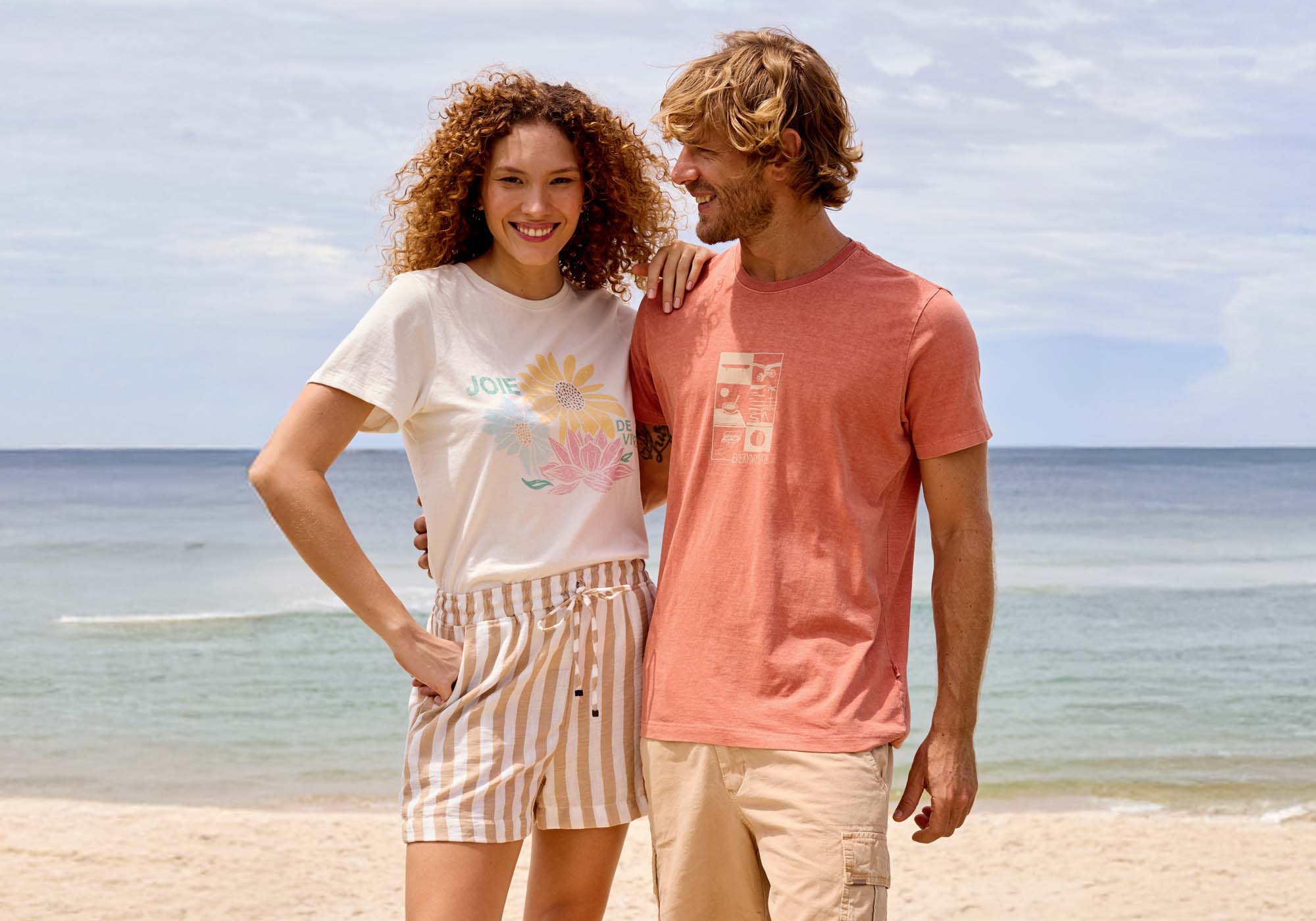 Casal sorridente na praia, roupas casuais de verão.